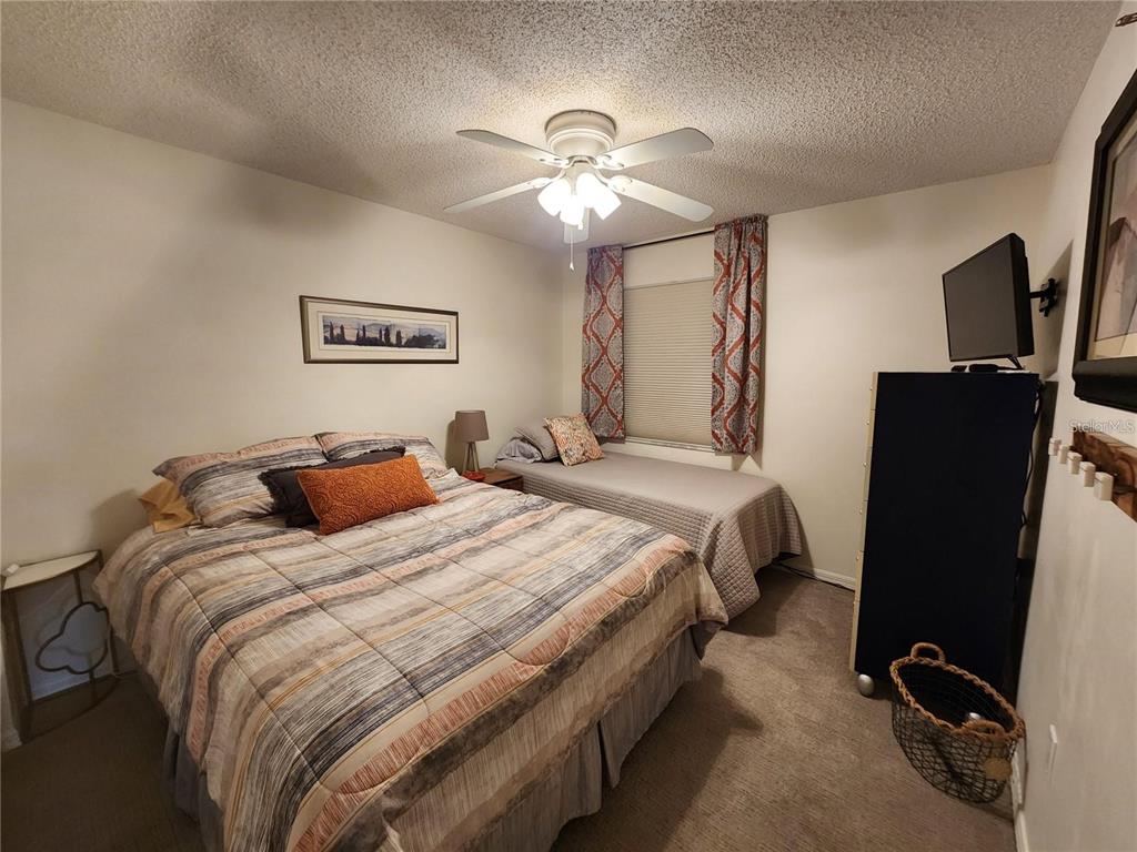 A bedroom features a queen bed, a twin bed, a ceiling fan, and carpeted flooring — 6505 STONE RIVER ROAD UNIT 203, BRADENTON, FL