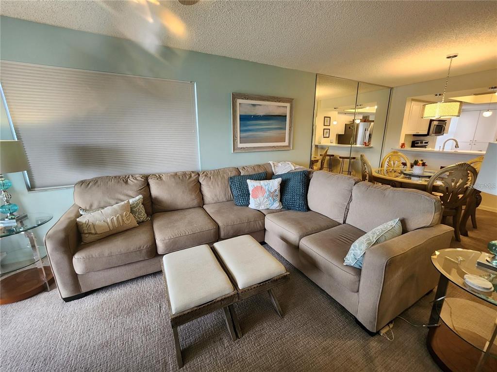 A living room features a large beige sectional sofa, two ottomans, and an adjacent dining area — 6505 STONE RIVER ROAD UNIT 203, BRADENTON, FL