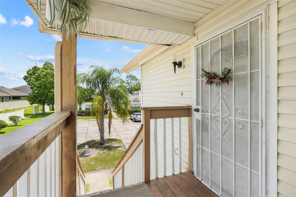 A view from a wooden porch looking down stairs toward a palm tree and driveway — 2734 RIO GRANDE TRAIL UNIT 2734, KISSIMMEE, FL