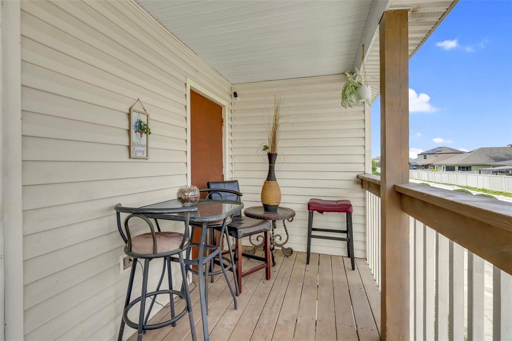A covered wooden balcony features a small bistro table, chairs, and a decorative wall sign — 2734 RIO GRANDE TRAIL UNIT 2734, KISSIMMEE, FL