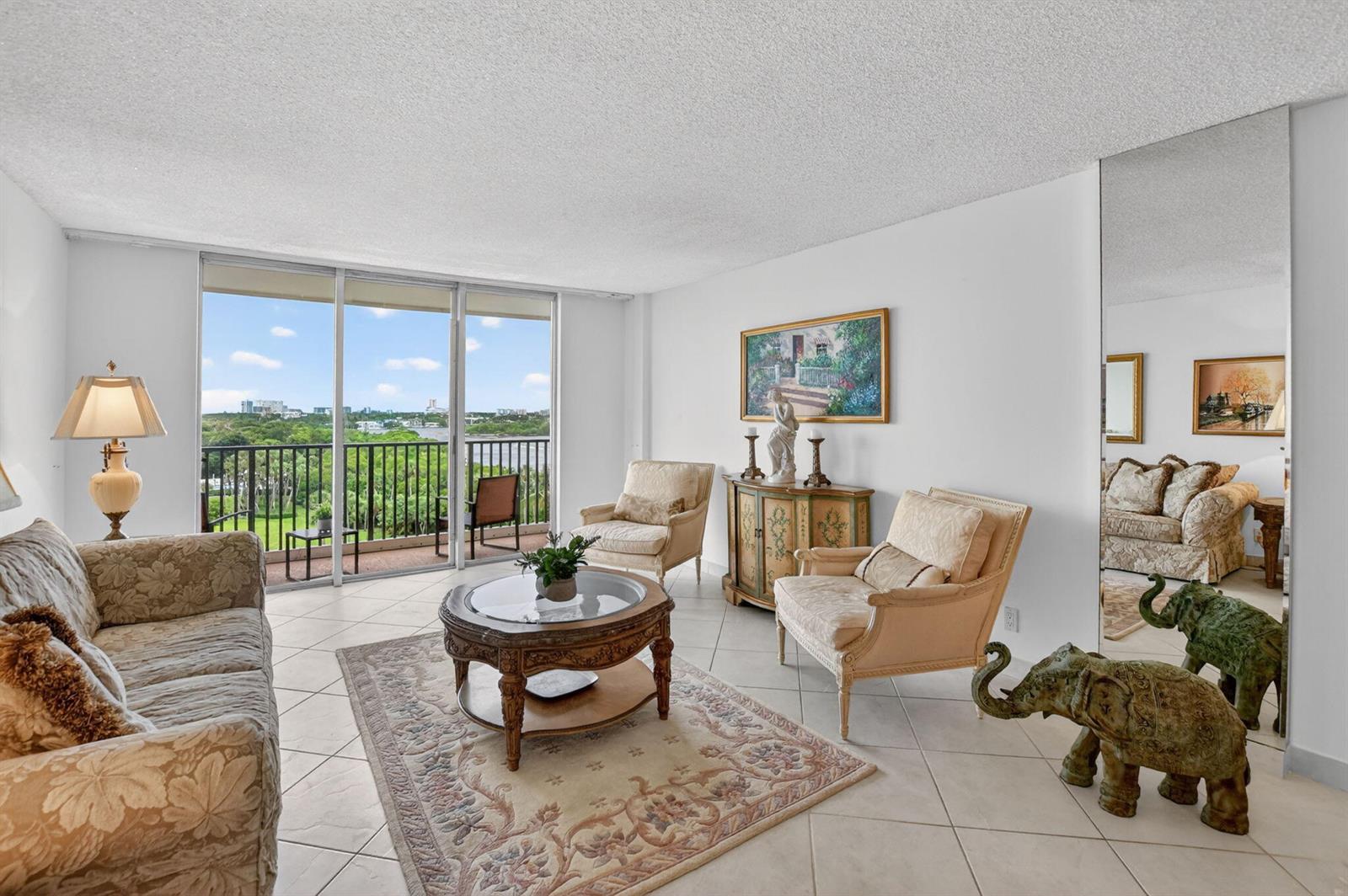 A living room with tile floors, a balcony view, patterned furniture, and a decorative elephant statue — 2121 N Ocean Boulevard # 805w, Boca Raton FL 33431, BOCA RATON, FL