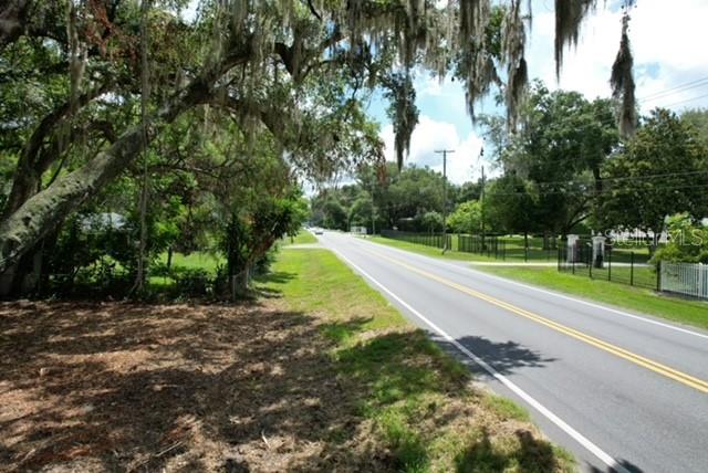 A paved road runs alongside a grassy area shaded by large, moss-covered oak trees — E HWY 25, OCKLAWAHA, FL