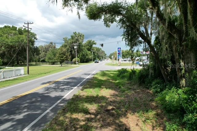 A paved road runs past a grassy lot with trees and a distant gas station sign — E HWY 25, OCKLAWAHA, FL