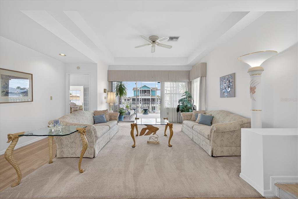 A living room features two beige sofas, glass-topped tables, and a sliding door to a balcony — 4340 SEAGULL DRIVE, NEW PORT RICHEY, FL