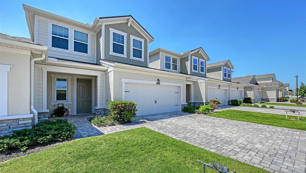 A row of two-story townhomes features beige stucco siding, stone accents, and paved driveways — 3693 DIVOT LANE, SARASOTA, FL