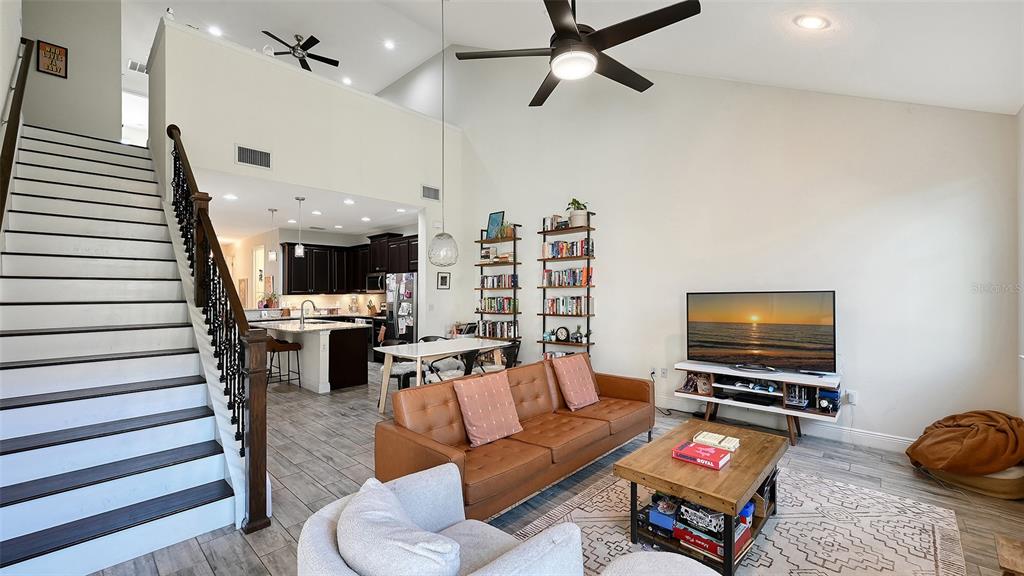 A living room with a staircase, vaulted ceiling, and an open kitchen in the background — 3693 DIVOT LANE, SARASOTA, FL
