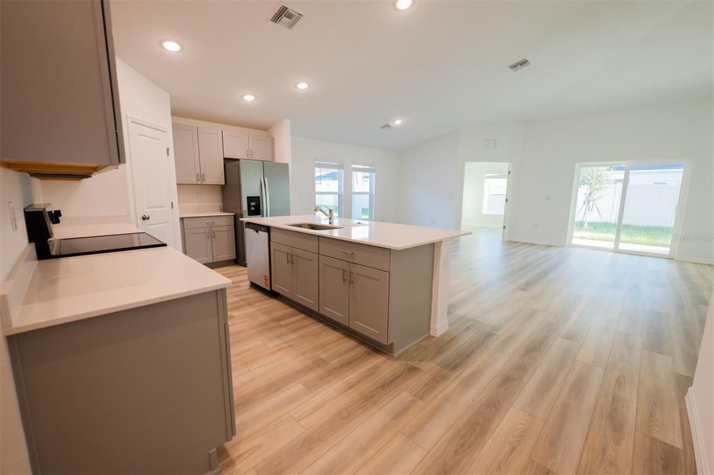 A modern kitchen features gray cabinets, white countertops, and an island overlooking an open living area — 4124 RIVER BEACON BOULEVARD, DAVENPORT, FL