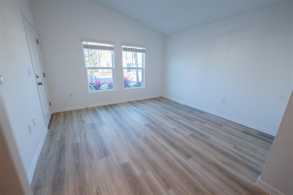 An empty room features light wood-look flooring, white walls, and two windows — 4124 RIVER BEACON BOULEVARD, DAVENPORT, FL