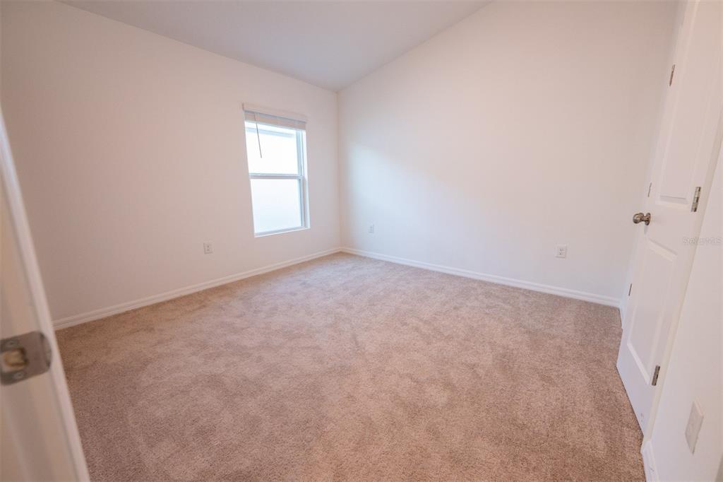 An empty bedroom features beige carpeting, white walls, and a single window — 4124 RIVER BEACON BOULEVARD, DAVENPORT, FL