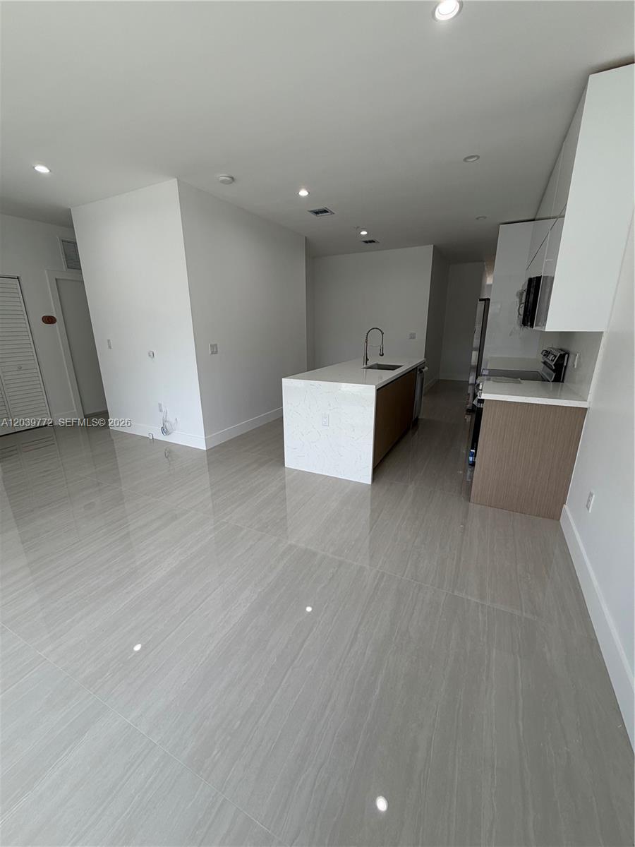 A modern kitchen features a white marble-topped island, light wood cabinetry, and glossy tile flooring — 9708 NW 26th Ave, Miami FL 33147, MIAMI, FL