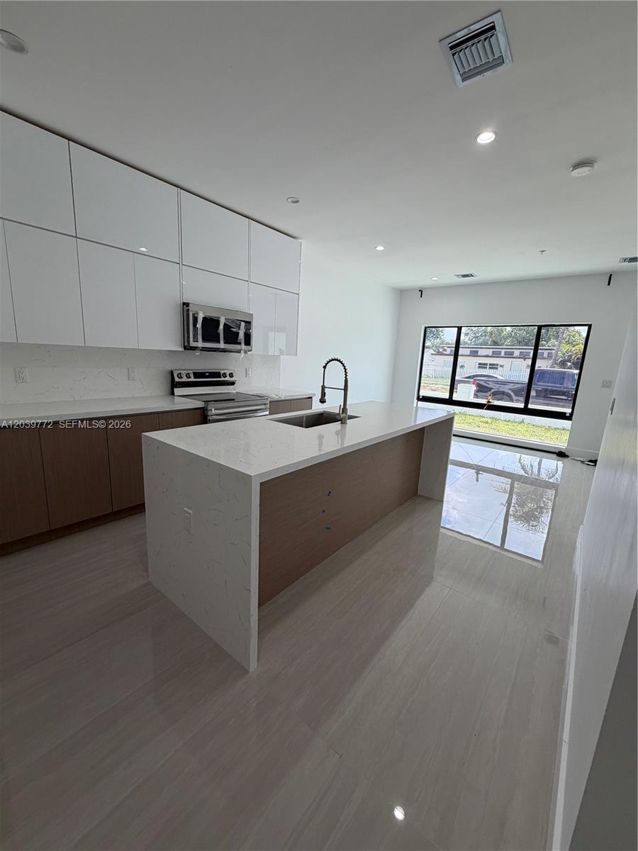 A modern kitchen features white upper cabinets, wood-toned lower cabinets, and a large quartz island — 9708 NW 26th Ave, Miami FL 33147, MIAMI, FL