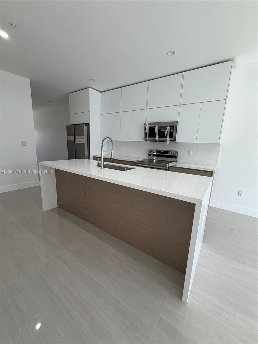 A modern kitchen features white upper cabinets, wood-tone lower cabinets, and a white quartz island — 9708 NW 26th Ave, Miami FL 33147, MIAMI, FL