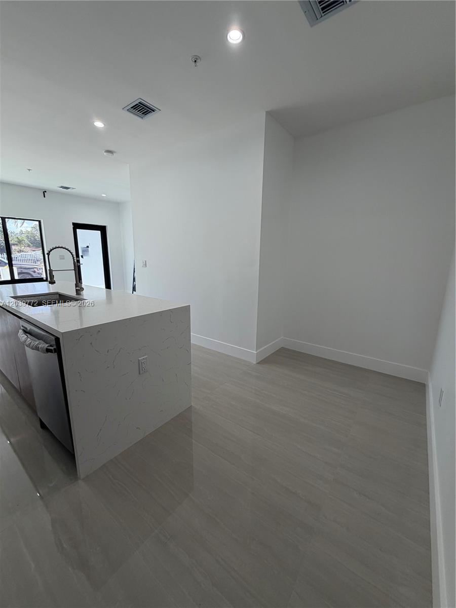 A modern kitchen features a white marble-topped island, light tile flooring, and white walls — 9708 NW 26th Ave, Miami FL 33147, MIAMI, FL