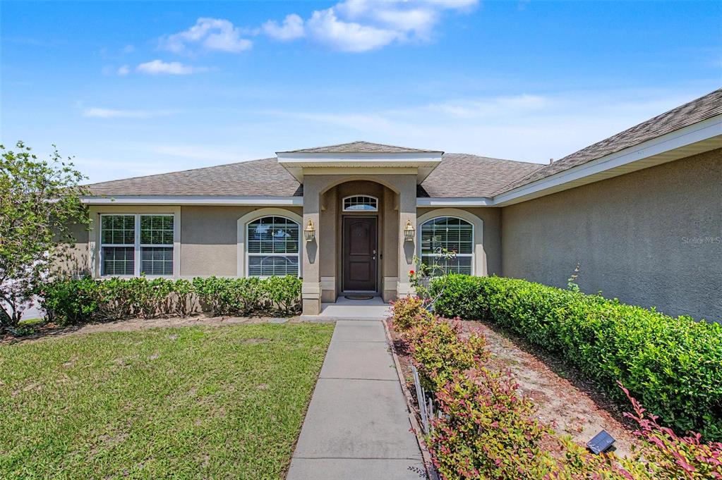 A single-story house exterior features a concrete walkway leading to a covered front entryway — 1621 DOVES VIEW CIRCLE, AUBURNDALE, FL