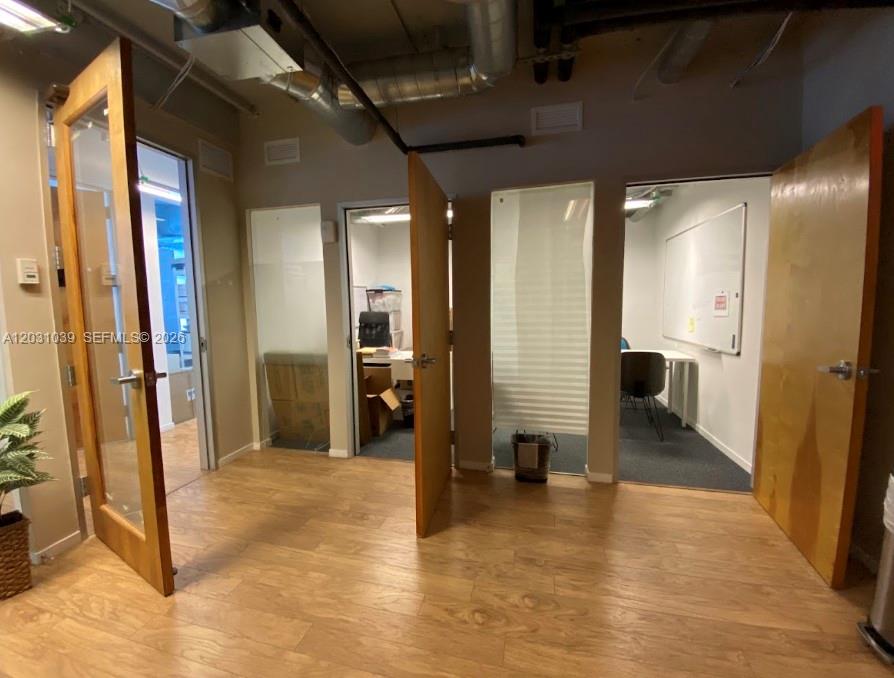 A hallway with wood-look flooring leads to three office doorways with exposed ceiling ductwork — 14 NE 1st Ave, Miami FL 33132, MIAMI, FL
