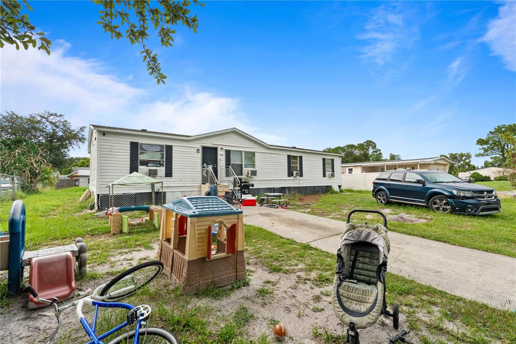A single-story manufactured home with a front yard containing various children's toys and a car — 14758 CONGRESS STREET, ORLANDO, FL