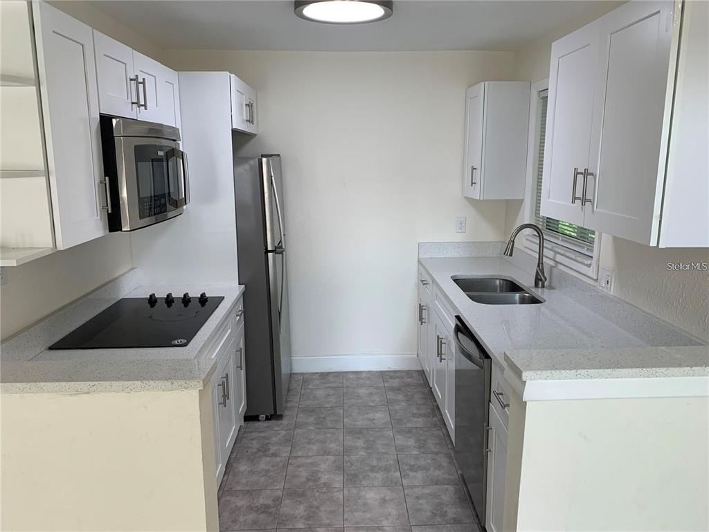 A galley kitchen features white cabinets, stainless steel appliances, and gray tiled flooring — 17202 SANDALWOOD DRIVE UNIT 202, WILDWOOD, FL