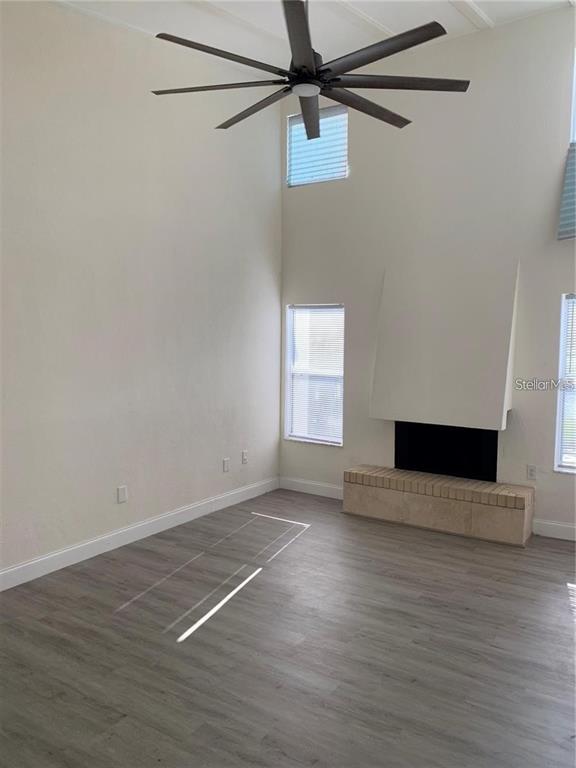 A living room with high ceilings, a ceiling fan, light wood flooring, and a fireplace — 17202 SANDALWOOD DRIVE UNIT 202, WILDWOOD, FL