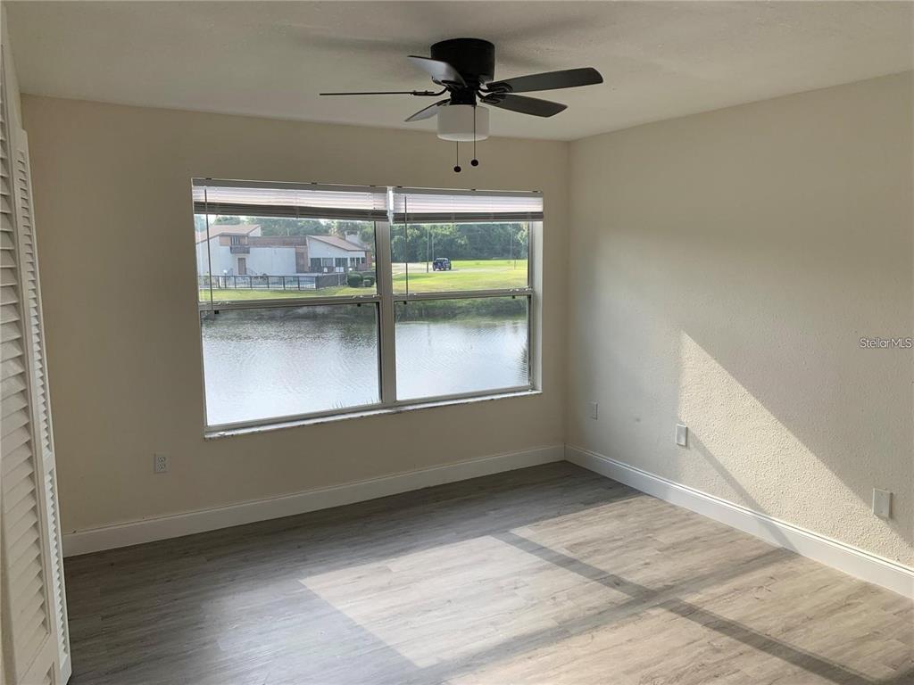 An empty bedroom with light wood-look flooring, a ceiling fan, and a view of water — 17202 SANDALWOOD DRIVE UNIT 202, WILDWOOD, FL