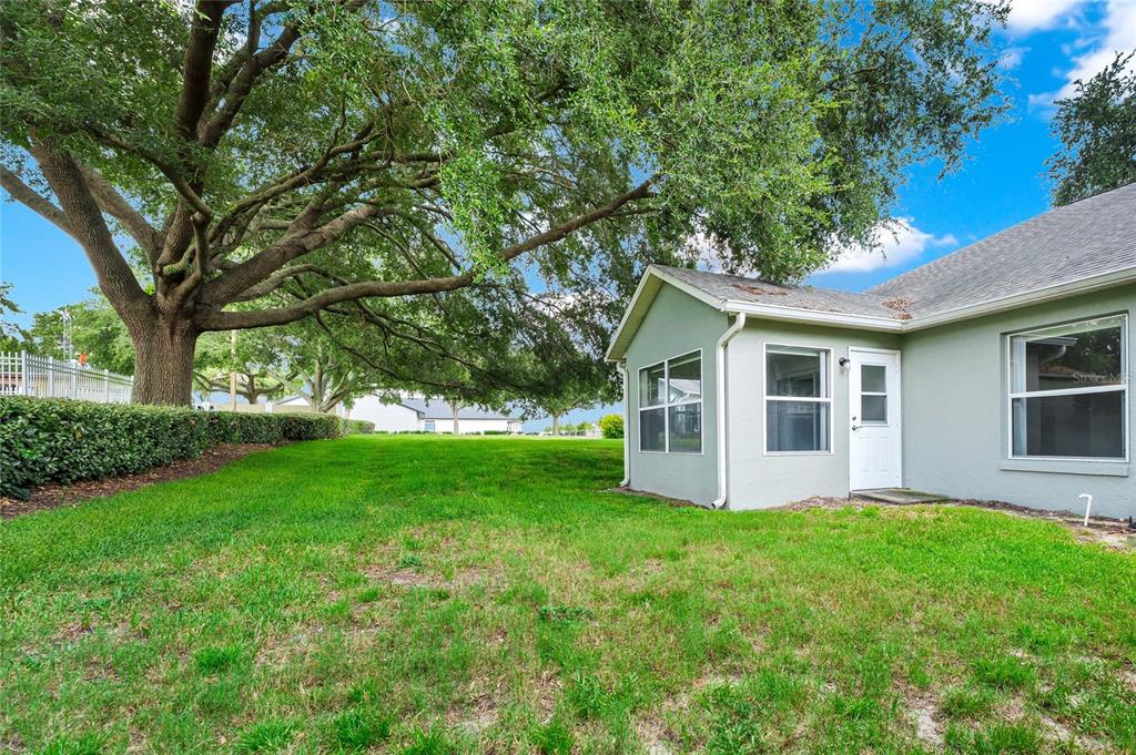 The exterior of a light-colored house features a side door and a large oak tree — 648 HARBOR VILLA COURT UNIT 648, CLERMONT, FL