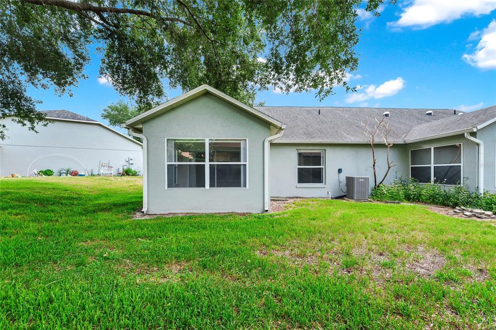 The exterior rear view of a single-story house features a grassy yard and trees — 648 HARBOR VILLA COURT UNIT 648, CLERMONT, FL