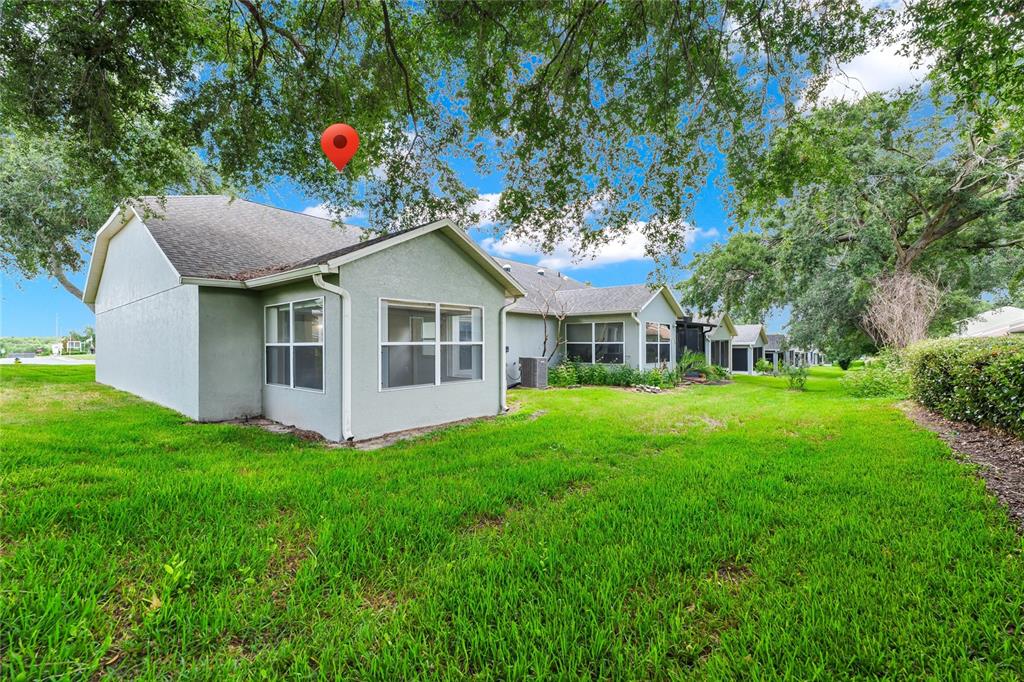 The exterior of a light-colored house with a grassy backyard and mature trees — 648 HARBOR VILLA COURT UNIT 648, CLERMONT, FL
