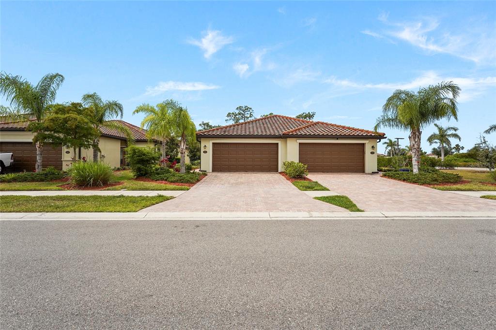 A street-level view of a duplex home with two brown garages and tiled roofs — 12055 AMICA LOOP, VENICE, FL