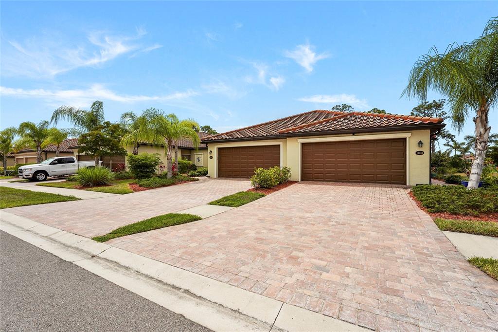 A single-story house with a tile roof, two garage doors, and a paved driveway — 12055 AMICA LOOP, VENICE, FL