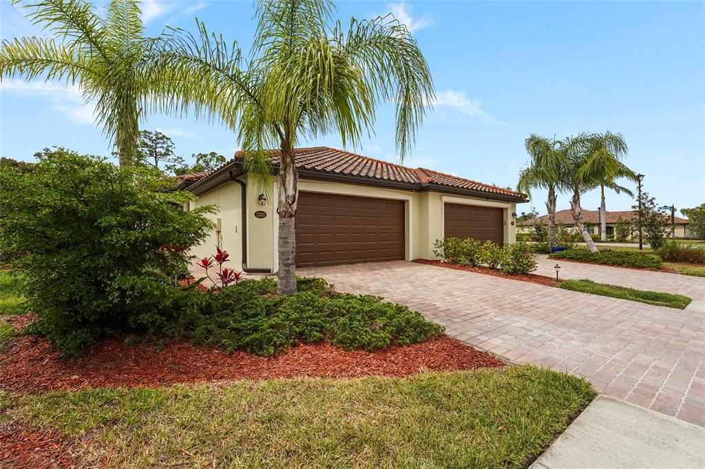 A single-story house with a two-car garage, a paved driveway, and palm trees — 12055 AMICA LOOP, VENICE, FL