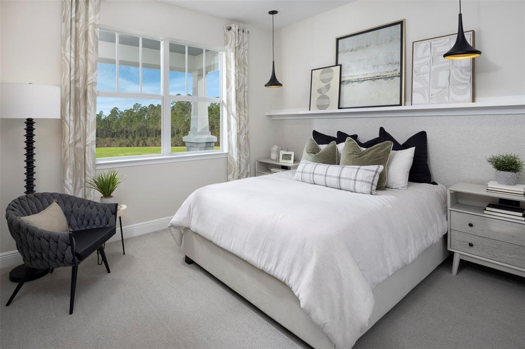 A bedroom features a queen bed, a gray armchair, and a window overlooking a forest — 18296 CHROMATA DRIVE, VENICE, FL