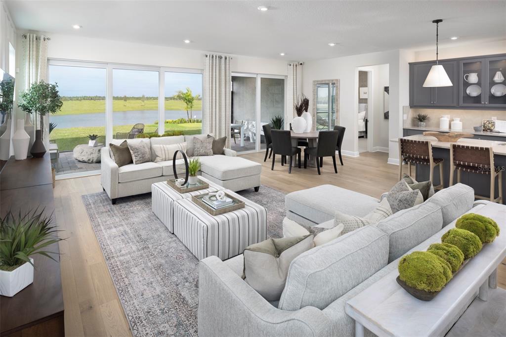 An open-concept living room and kitchen feature light wood floors, neutral furniture, and large windows — 18296 CHROMATA DRIVE, VENICE, FL