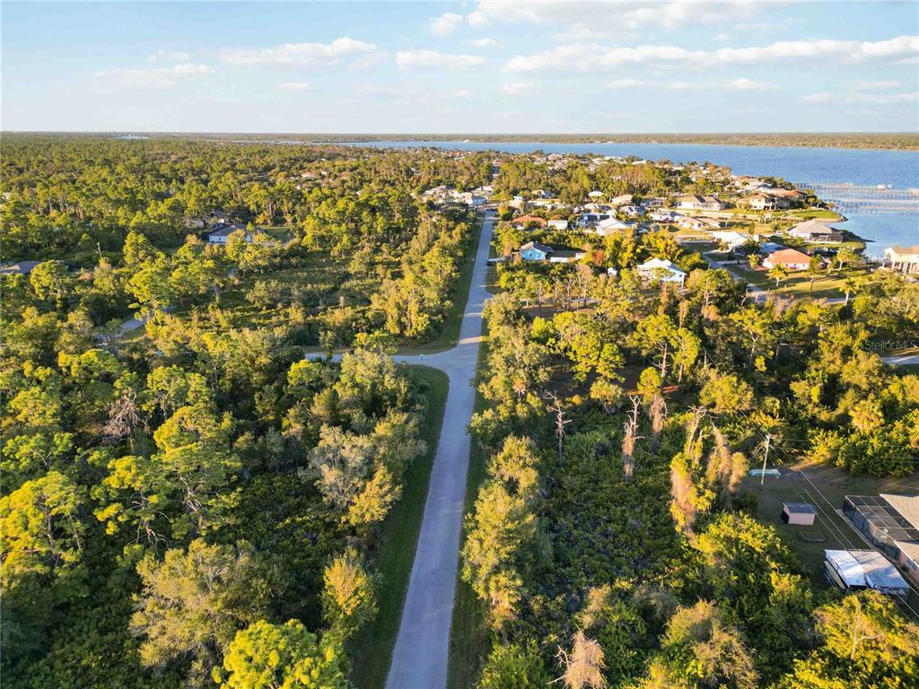 An aerial view shows a paved road leading toward a waterfront neighborhood surrounded by trees — 3552 DWIGHT STREET, PORT CHARLOTTE, FL