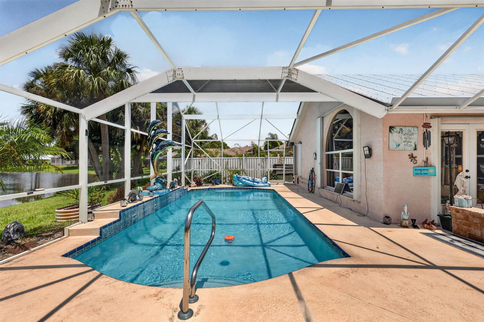 A screened-in swimming pool with a metal railing and a view of a pond — 1921 NE Acapulco Drive, Jensen Beach FL 34957, JENSEN BEACH, FL