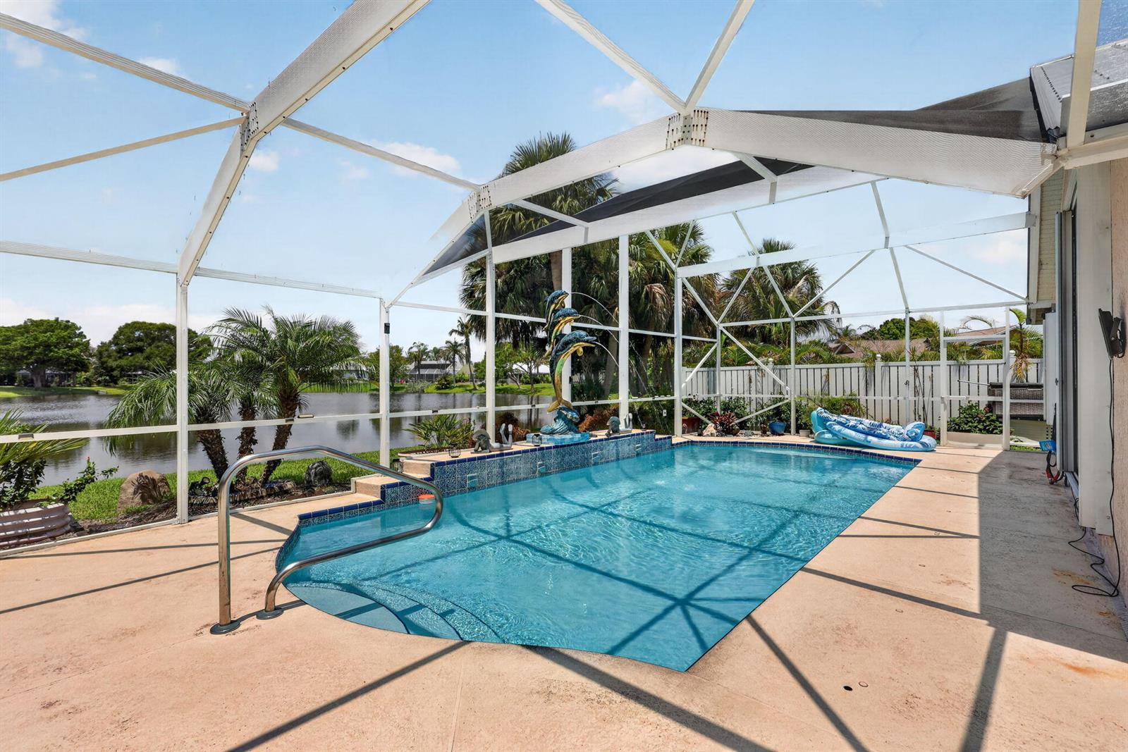 A swimming pool with a dolphin fountain sits inside a screened enclosure overlooking a lake — 1921 NE Acapulco Drive, Jensen Beach FL 34957, JENSEN BEACH, FL
