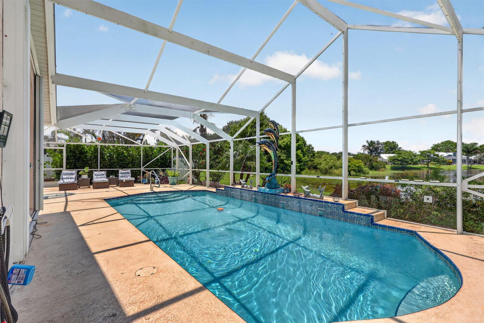 A screened-in swimming pool with a dolphin fountain overlooks a lake and green landscape — 1921 NE Acapulco Drive, Jensen Beach FL 34957, JENSEN BEACH, FL
