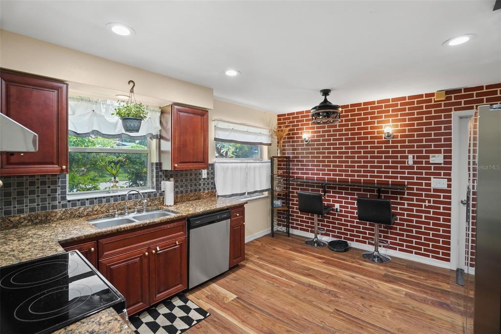 A kitchen with wood cabinets, granite countertops, and a red brick accent wall with bar seating — 1564 SANTA MONICA DRIVE, DUNEDIN, FL