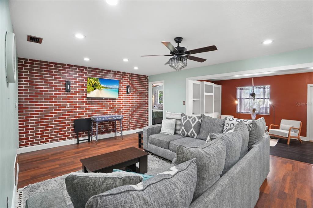 A living room features a brick accent wall, gray sectional sofa, and dark wood flooring — 1564 SANTA MONICA DRIVE, DUNEDIN, FL