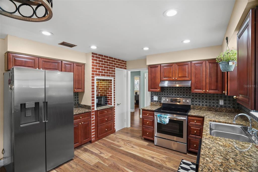 A kitchen with wood cabinets, stainless steel appliances, granite countertops, and a brick accent wall — 1564 SANTA MONICA DRIVE, DUNEDIN, FL