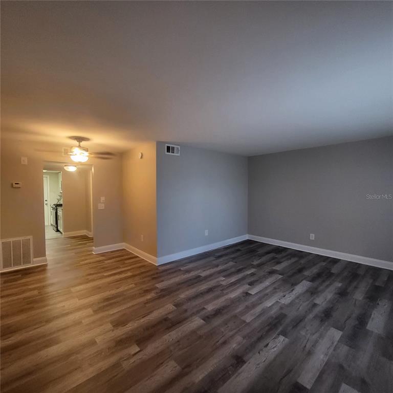 An empty living room features gray walls, wood-look flooring, and a doorway leading to a kitchen — 911 WASHINGTON AVENUE UNIT 218, LARGO, FL