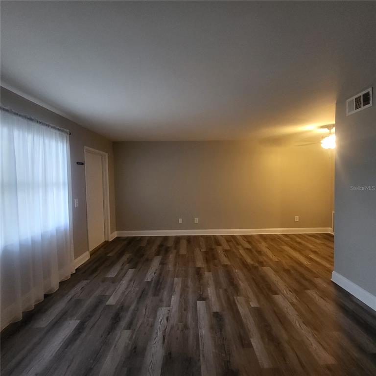 An empty room features gray walls, wood-look flooring, a window with white curtains, and a ceiling fan — 911 WASHINGTON AVENUE UNIT 218, LARGO, FL