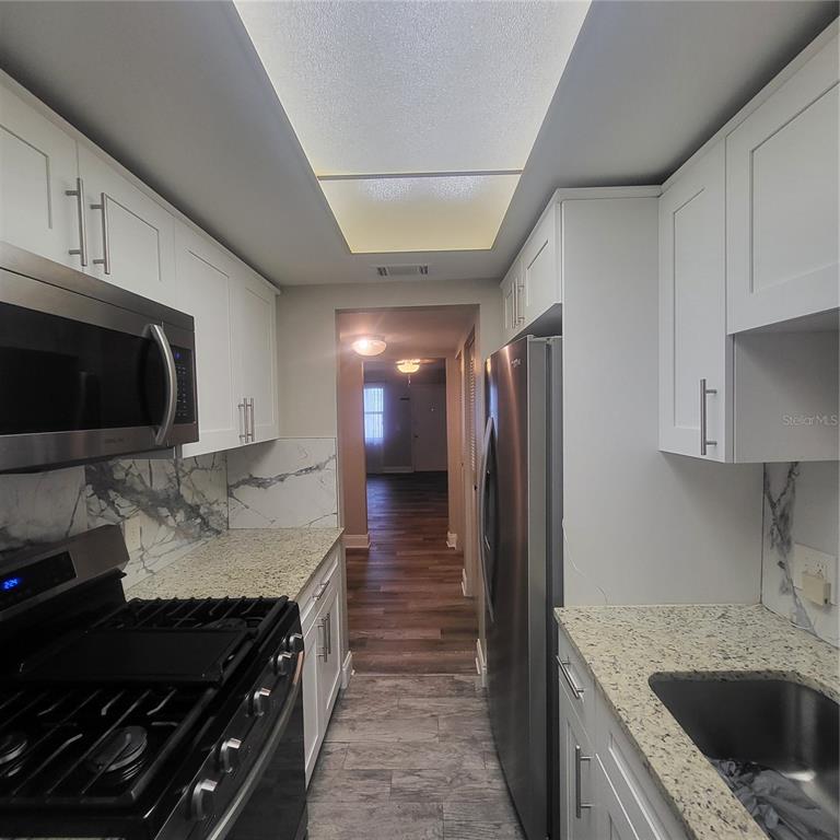 A galley kitchen features white cabinets, granite countertops, stainless steel appliances, and marble-look backsplashes — 911 WASHINGTON AVENUE UNIT 218, LARGO, FL