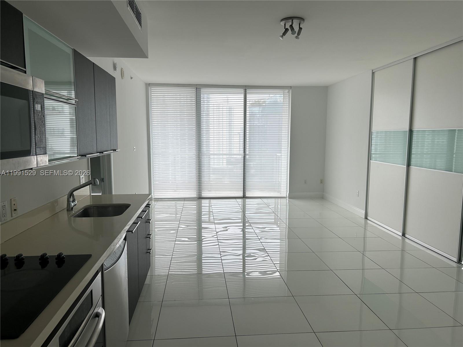 A modern kitchen with dark cabinets and white tile floors opens into a bright living area — 90 SW 3rd St # 3610, Miami FL 33130, MIAMI, FL