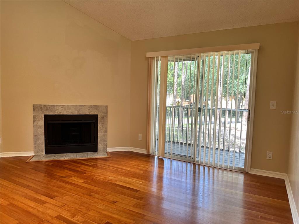 A living room with hardwood floors, a tiled fireplace, and sliding glass doors to a deck — 6052 WESTGATE DRIVE UNIT 203, ORLANDO, FL
