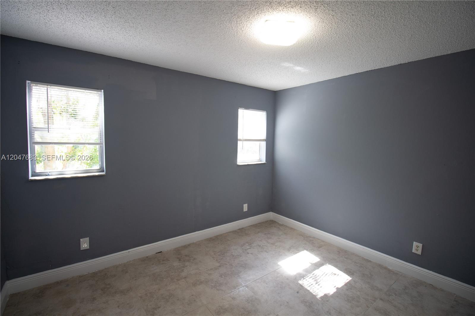 An empty bedroom features gray walls, tile flooring, and two windows with white blinds — 825 SW 10th St # B, Hallandale Beach FL 33009, HALLANDALE BEACH, FL