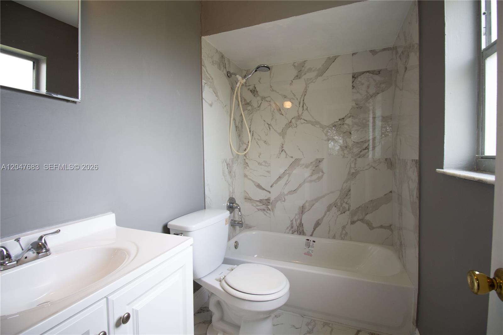 A bathroom features a white vanity, a toilet, and a bathtub with marble-patterned tile walls — 825 SW 10th St # B, Hallandale Beach FL 33009, HALLANDALE BEACH, FL