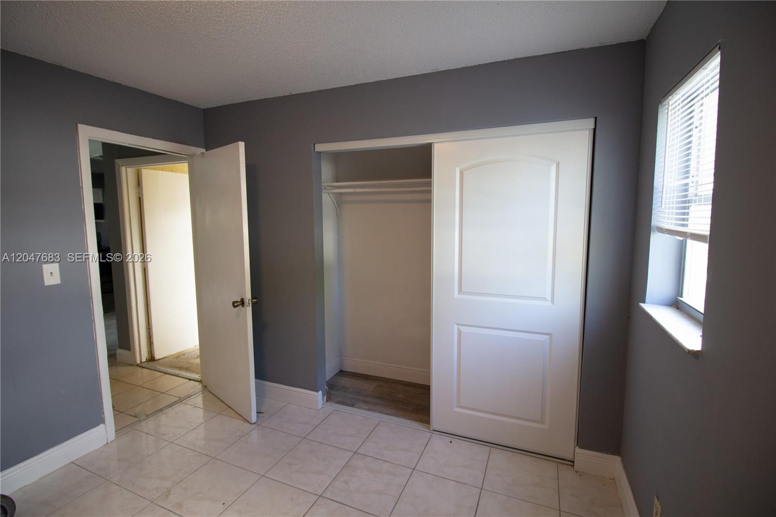 A bedroom features gray walls, white tile flooring, a closet, and a window with blinds — 825 SW 10th St # B, Hallandale Beach FL 33009, HALLANDALE BEACH, FL