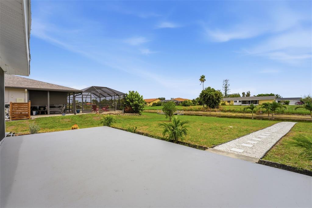 A concrete patio overlooks a grassy backyard with a canal and neighboring houses — 192 ANNAPOLIS LANE, ROTONDA WEST, FL