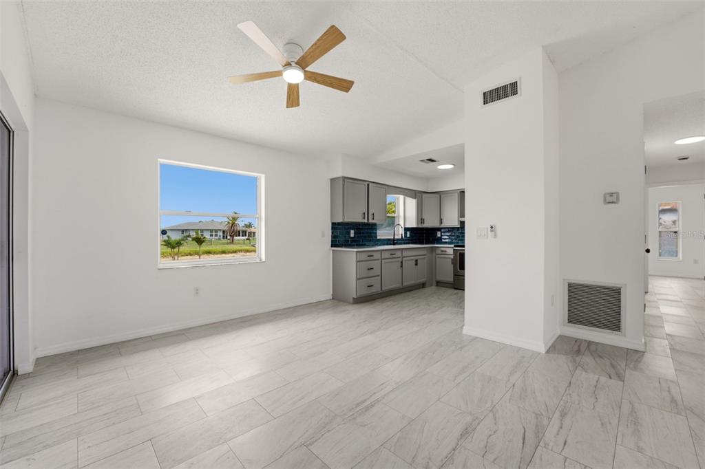 A bright kitchen with gray cabinets and blue tile backsplash opens into a tiled room — 192 ANNAPOLIS LANE, ROTONDA WEST, FL