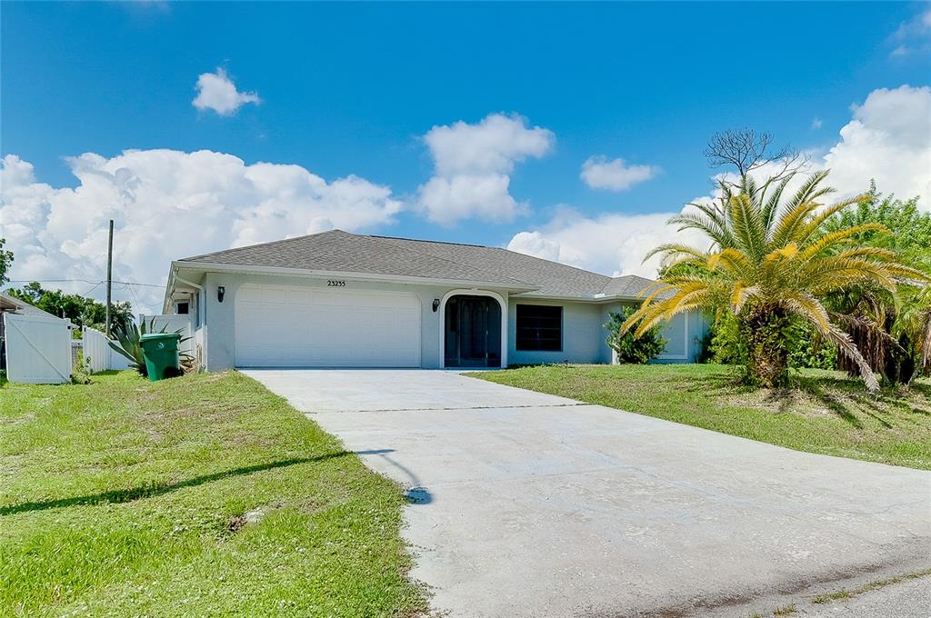 A single-story house with a white garage, arched entryway, and a palm tree in front — 23235 MCQUEENEY AVENUE, PUNTA GORDA, FL