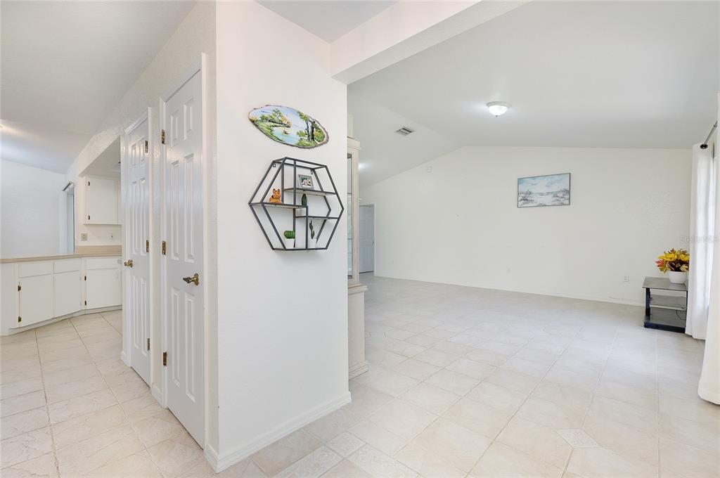 A white-walled living area with tile flooring, a hexagonal wall shelf, and an adjacent kitchen — 23235 MCQUEENEY AVENUE, PUNTA GORDA, FL